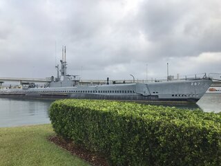 A historic submarine in the harbor of Pearl Harbor, Hawaii, under a cloudy sky.