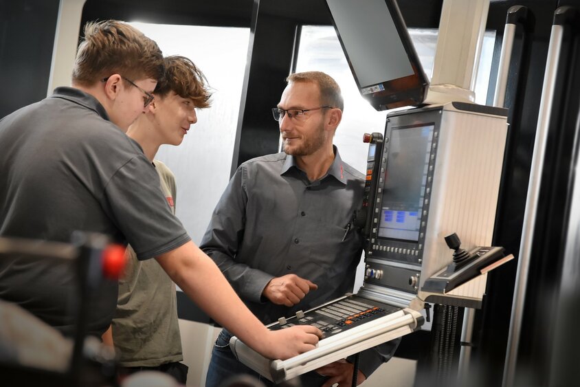 Ein Lehrlingsausbilder erklärt zwei Lehrlingen im Bereich Metalltechnik, Modul H8 Zerspanungstechnik, die Steuerung eines Bearbeitungszentrums.