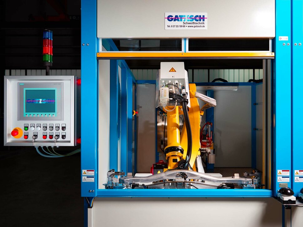 An automated joining system by Gatzsch Welding Technology featuring a yellow industrial robot performing precise welding tasks. On the left side, there is a control panel with a display monitoring the ongoing operation. The system is located in an industrial production environment, symbolizing the use of modern automation in joining technology.