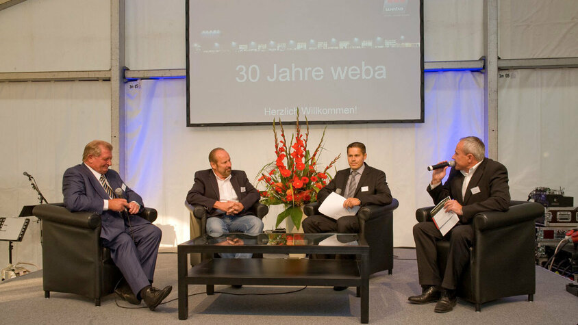 Unternehmensgründer Danzinger Herbert und Wolfgang Haidenthaler sowie Geschäftsführer Hannes Feuerhuber gemeinsam mit dem Event-Moderator auf der Bühne bei der 30-Jährigen Jubiläumsfeier, vor feierlichem Hintergrund. 