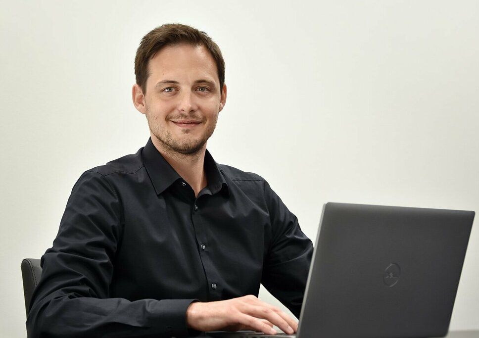 Ondrej Zima, Human Resource Manager der weba Olomouc sitzt avor einem geöffneten Laptop und  lächelt in die Kamera