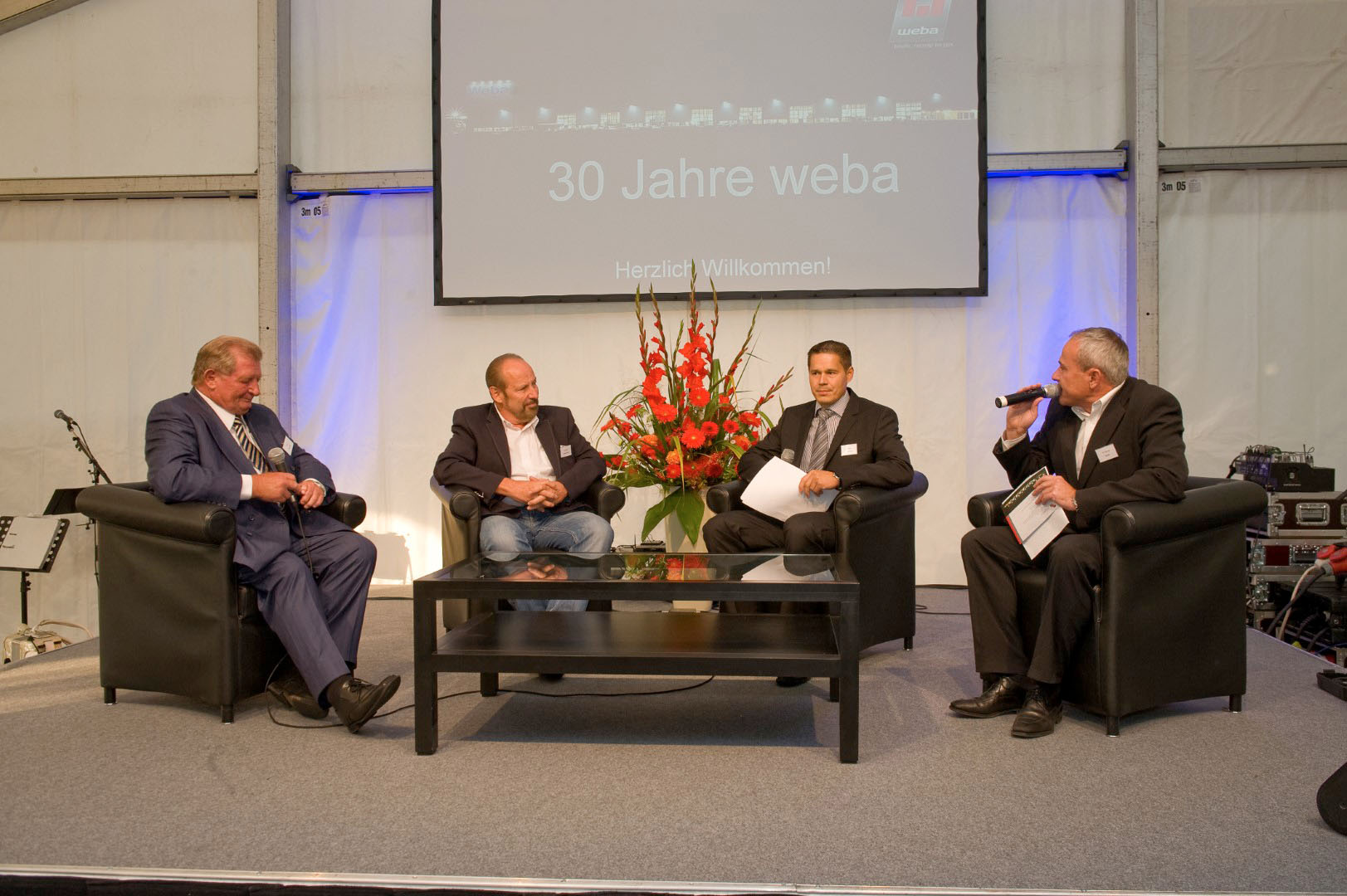 Unternehmensgründer Danzinger Herbert und Wolfgang Haidenthaler sowie Geschäftsführer Hannes Feuerhuber gemeinsam mit dem Event-Moderator auf der Bühne bei der 30-Jährigen Jubiläumsfeier, vor feierlichem Hintergrund. 